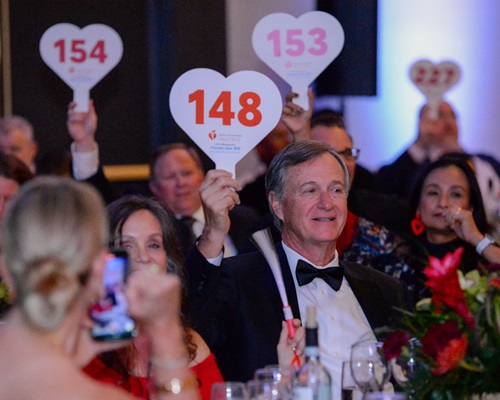 Crowd of people holding up heart-shaped bidder paddles.